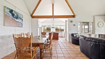 A spacious living area with a wooden dining table and chairs, a black leather sofa, and a kitchen in the background.