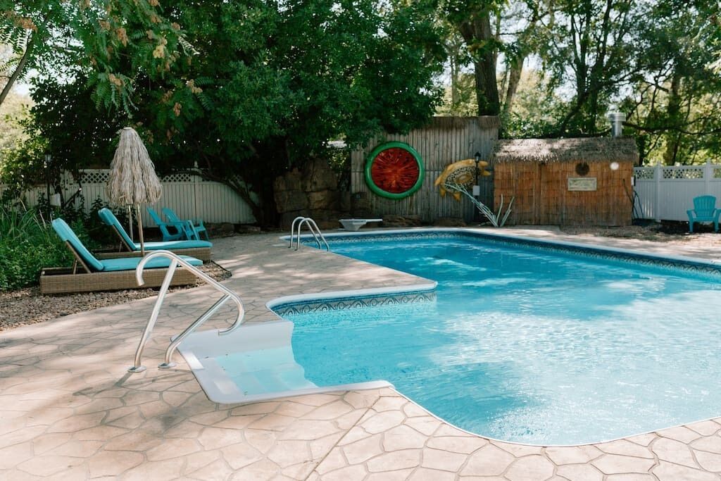 Une piscine dotée d’une terrasse en pierre, de chaises longues et d’une structure en bois.