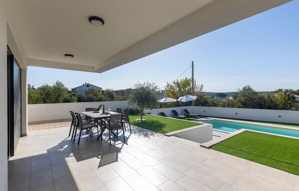 A modern outdoor patio with a pool, seating area, and a view of the surrounding landscape.