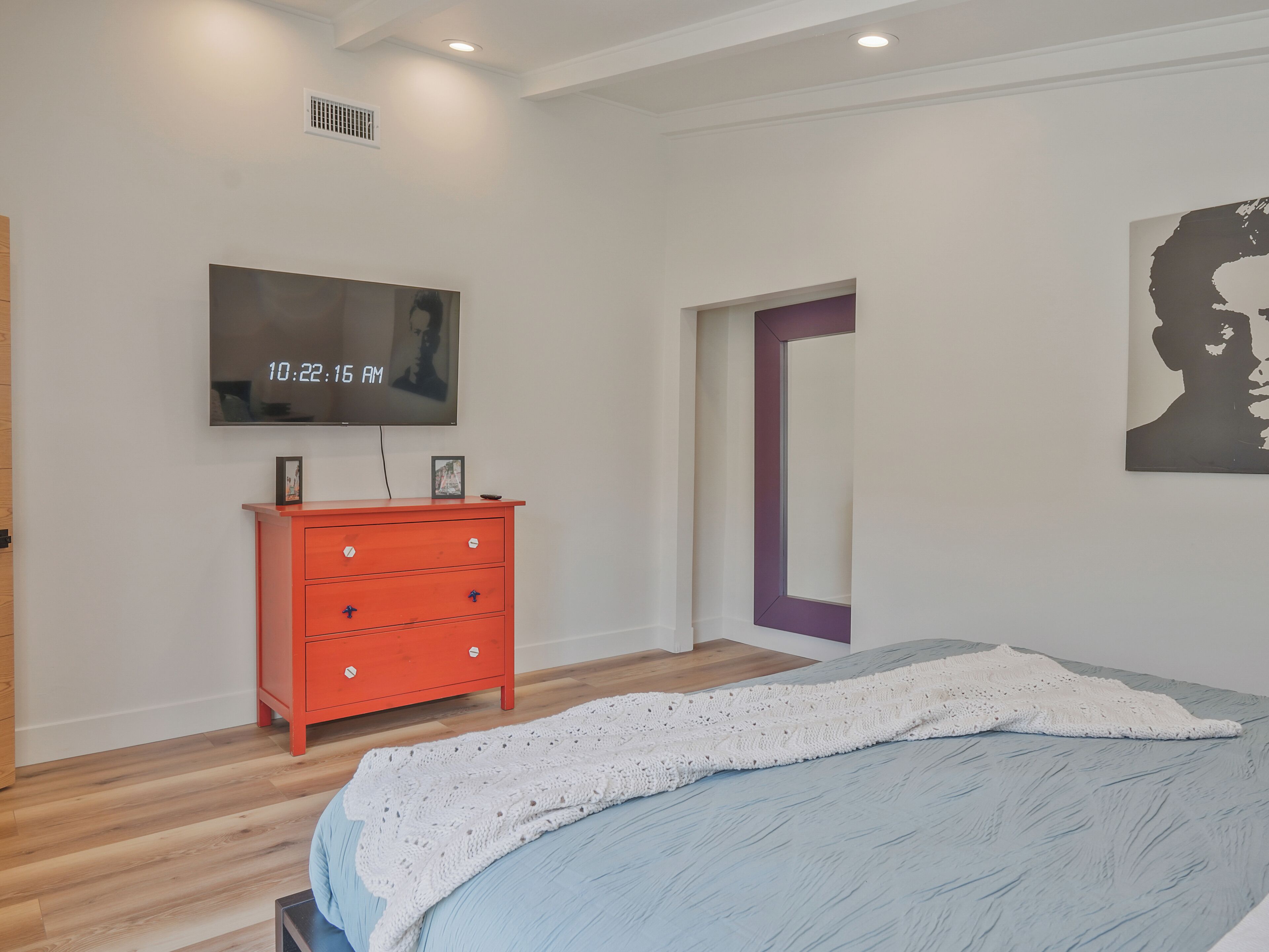 A bedroom with a bed, a TV, a red dresser, and a door.