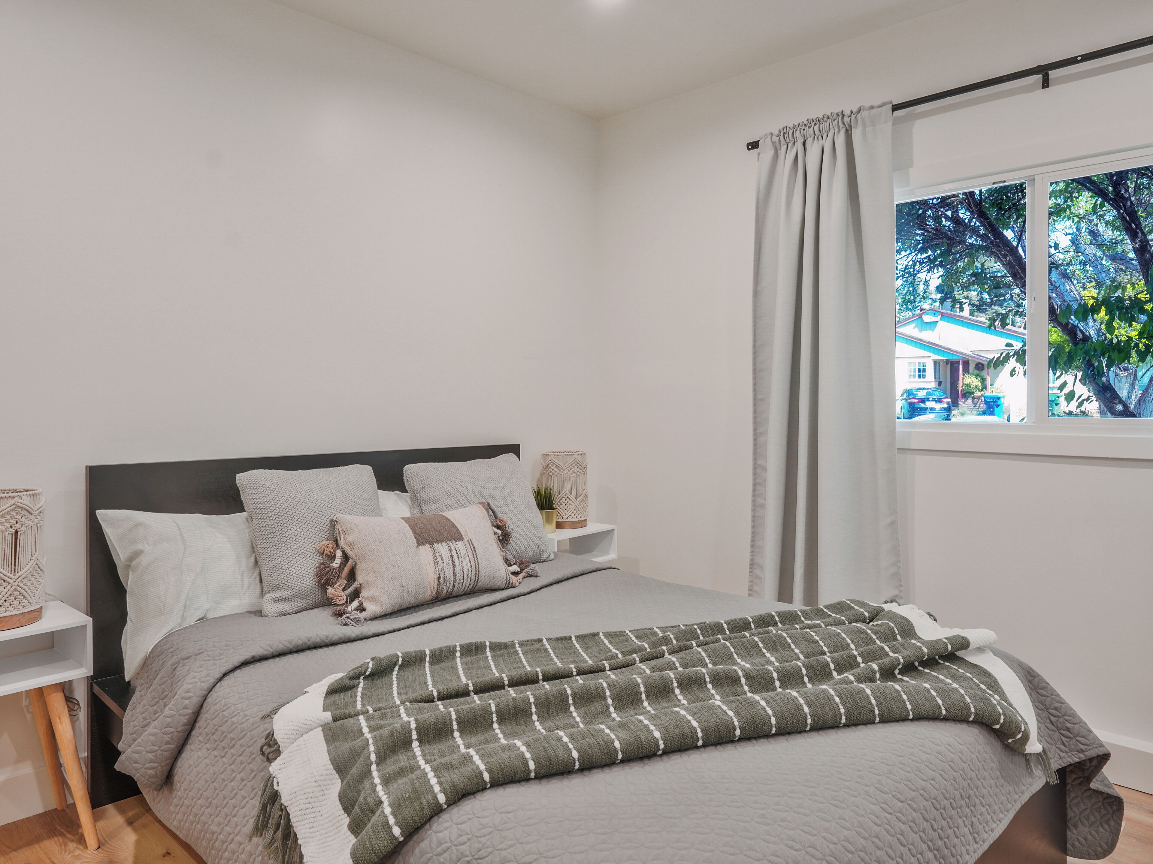 A neatly arranged bedroom with a bed, pillows, a bedside table, and a window with a view of the outside.