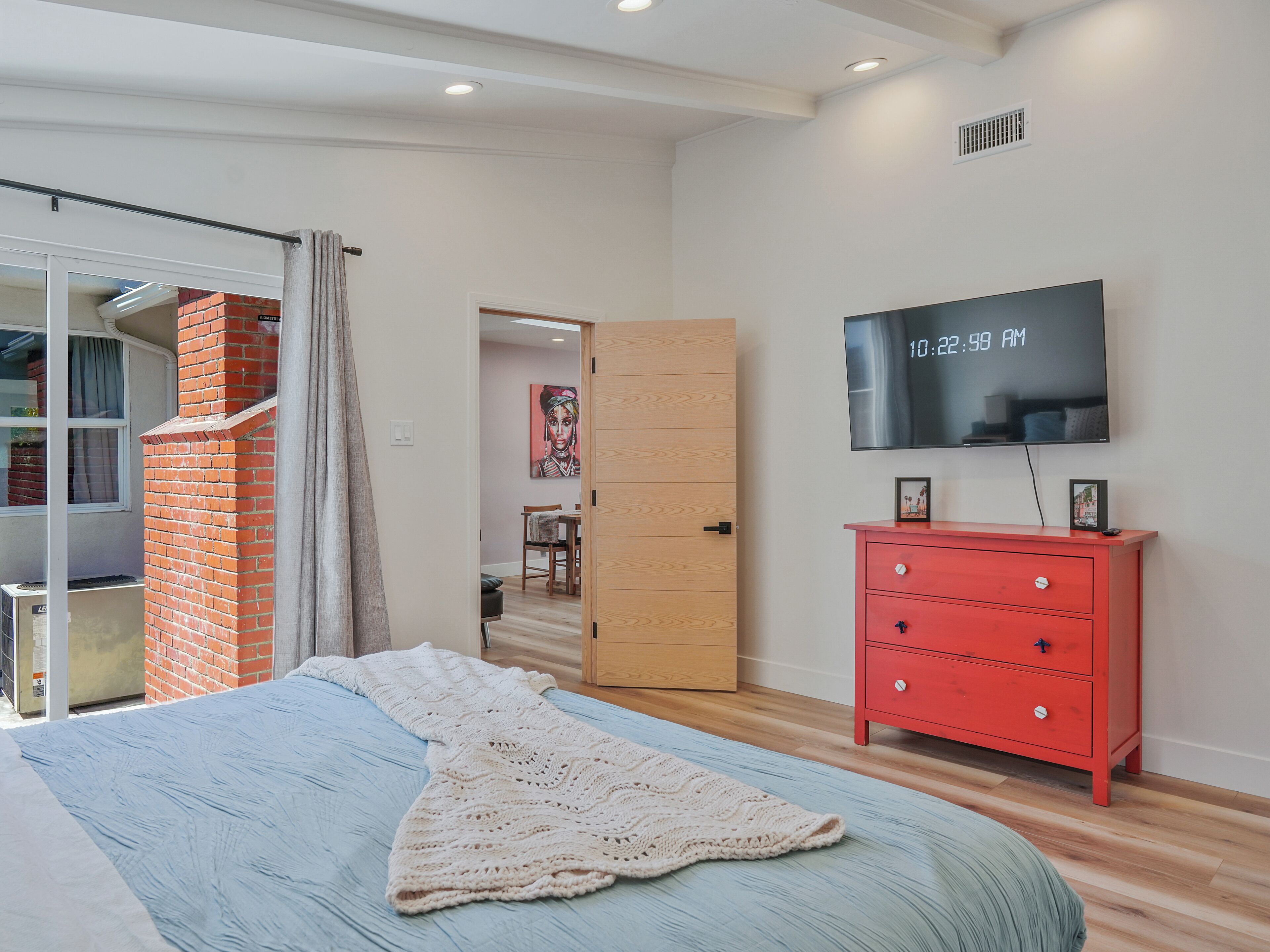 Un dormitorio con cama, un aparador rojo, un televisor y una puerta que da a un comedor.