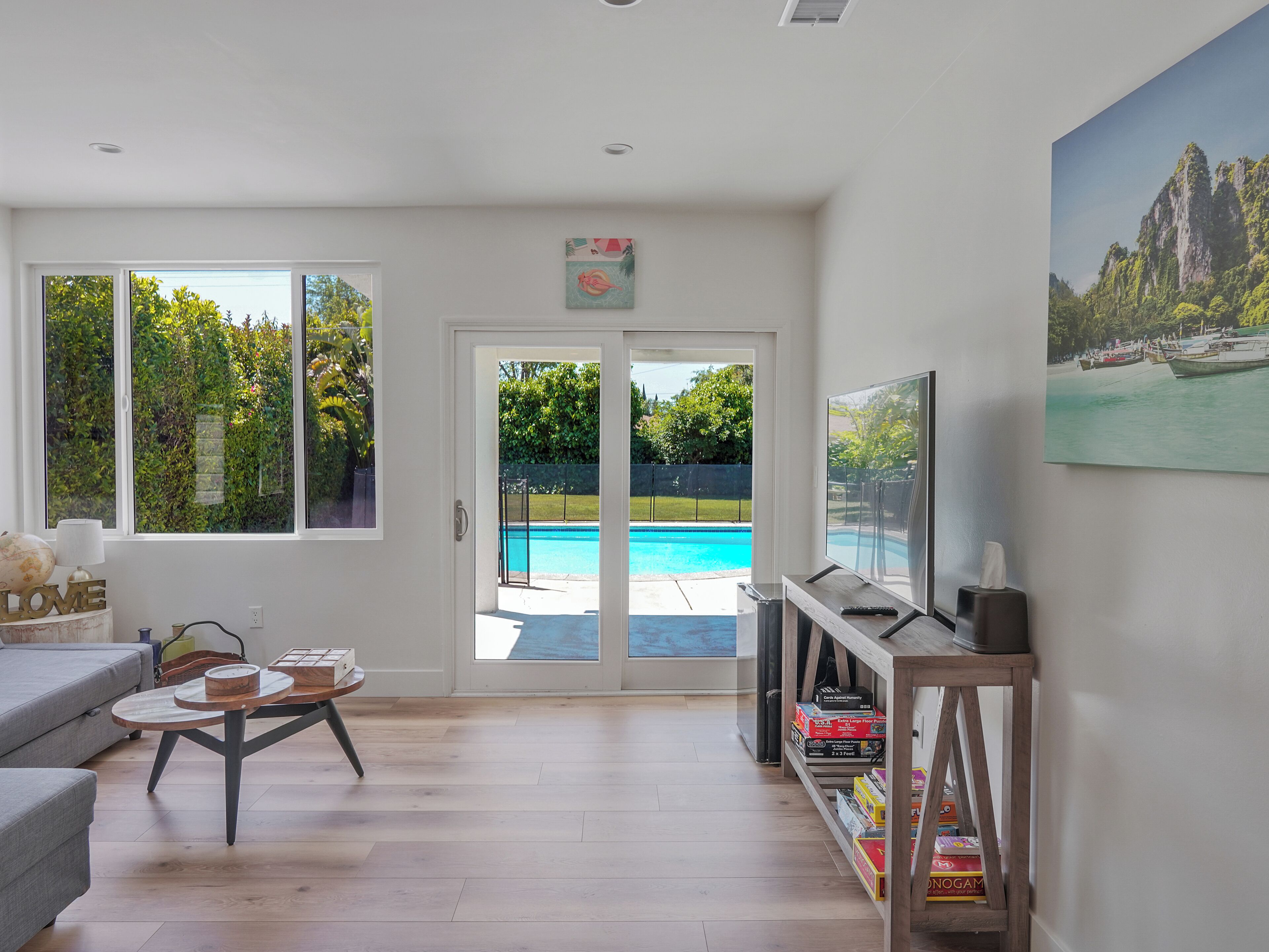 Un salon spacieux avec une grande fenêtre, une piscine et un tableau représentant un paysage montagneux.