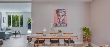 A modern dining area with a wooden table, benches, and a painting on the wall.