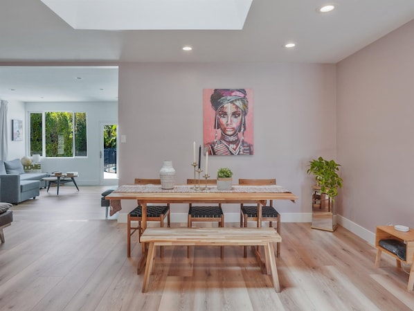 A modern dining area with a wooden table, benches, and a painting on the wall. - Hollywood Dream Remodeled Pool & Jacuzzi (Van Nuys)