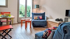A room with a wooden table, a blue chair, a sofa, and a bed.