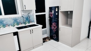 Una cucina con mobili bianchi, un frigorifero nero decorato con motivi floreali e una finestra con un murale a tema marino.