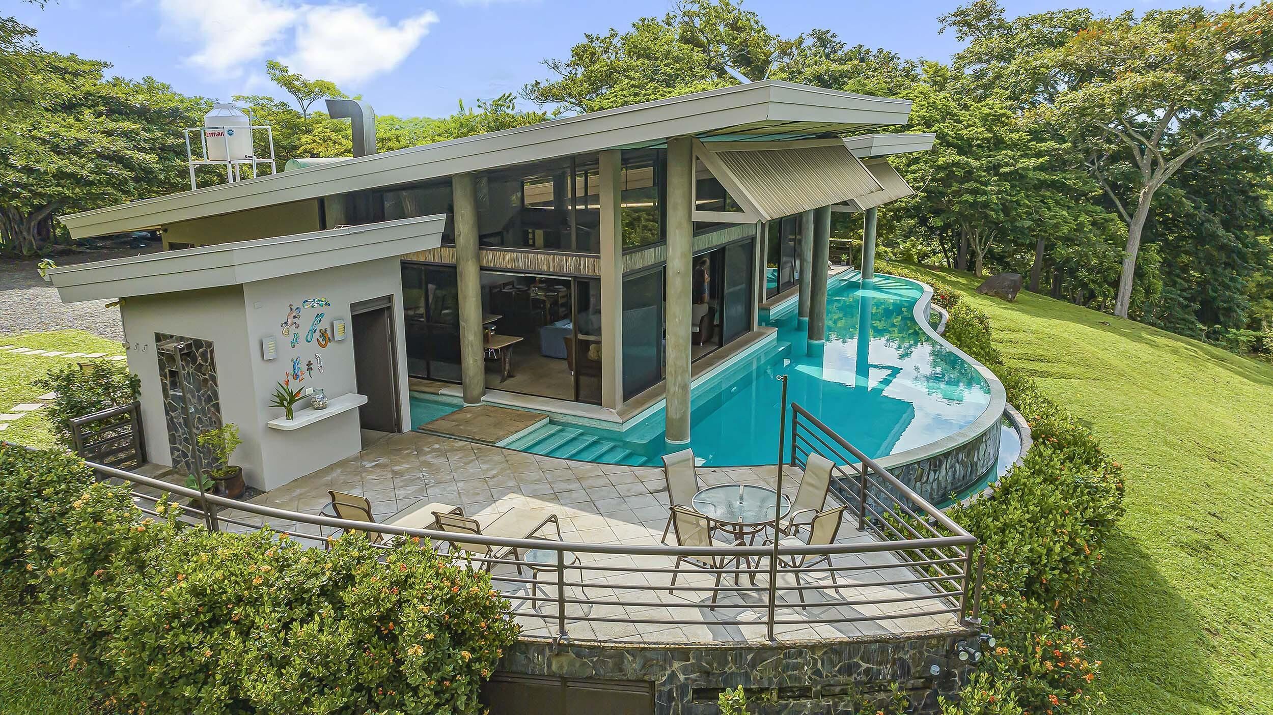 Una casa moderna con piscina, mobiliario exterior y un porche cubierto.