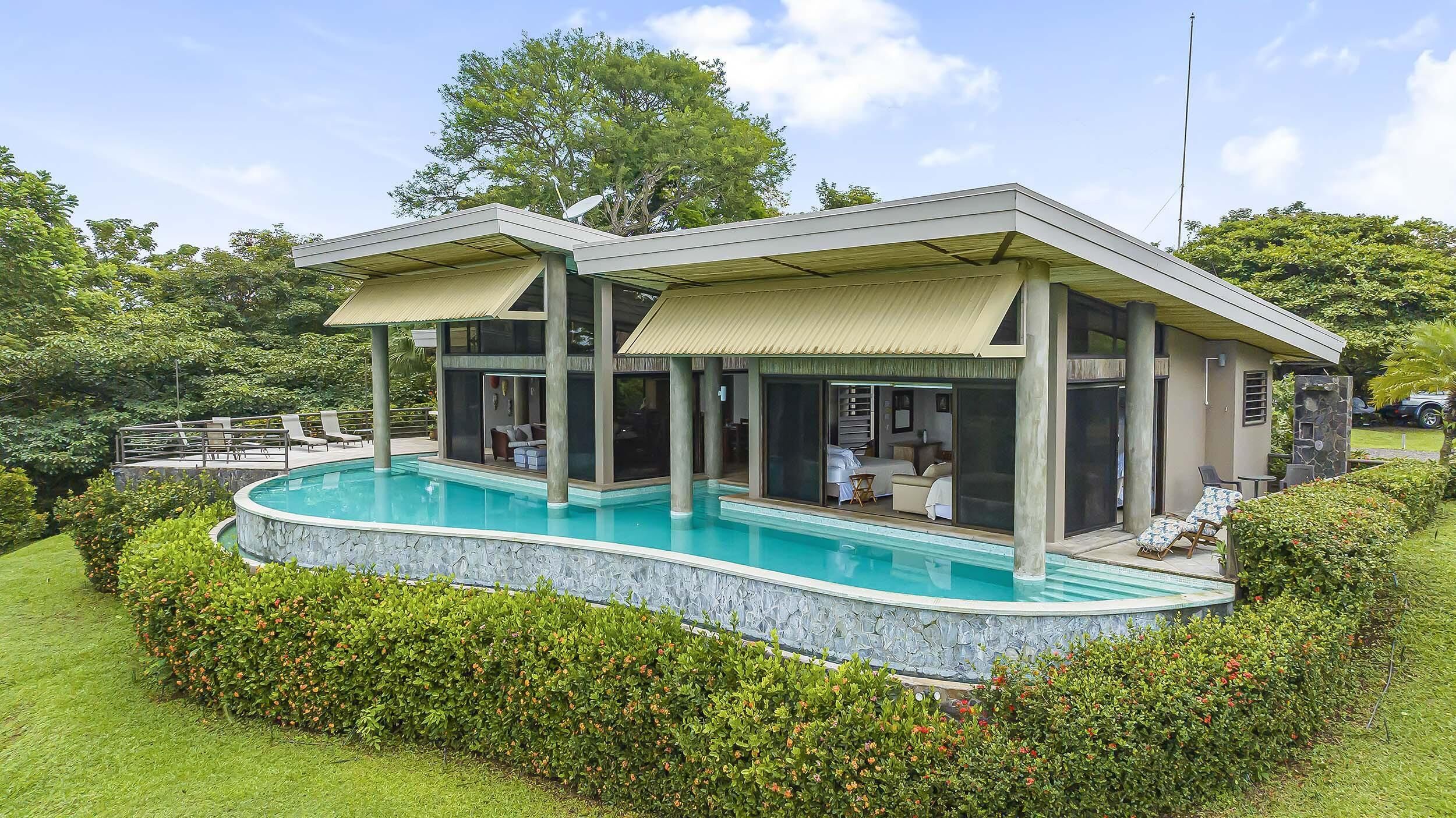 Ein modernes, zweistöckiges Haus mit Swimmingpool, großen Fenstern und Sitzgelegenheit im Freien.
