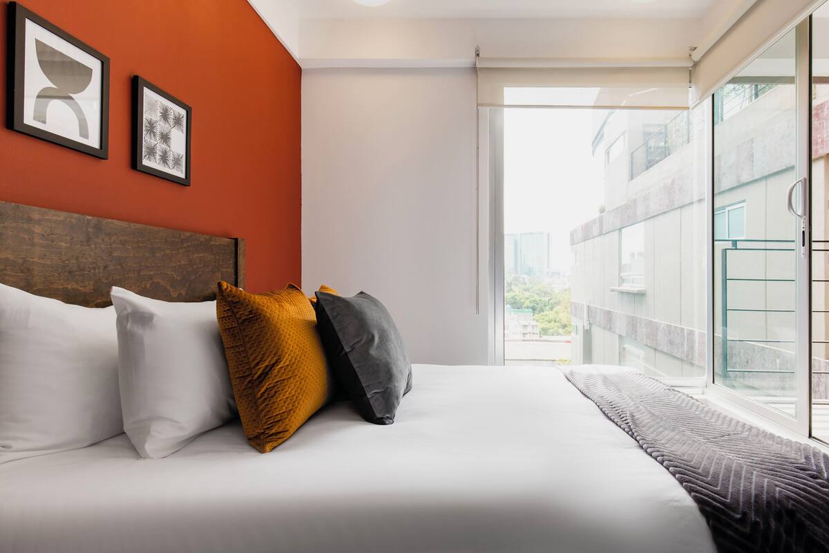 A hotel room with a bed, pillows, and two framed pictures on the wall.