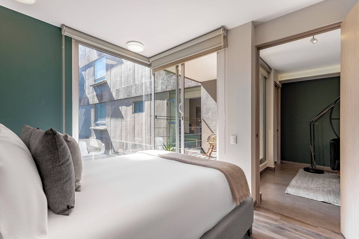 A bedroom with a large bed, a sliding glass door leading to a balcony, and a staircase to another room.