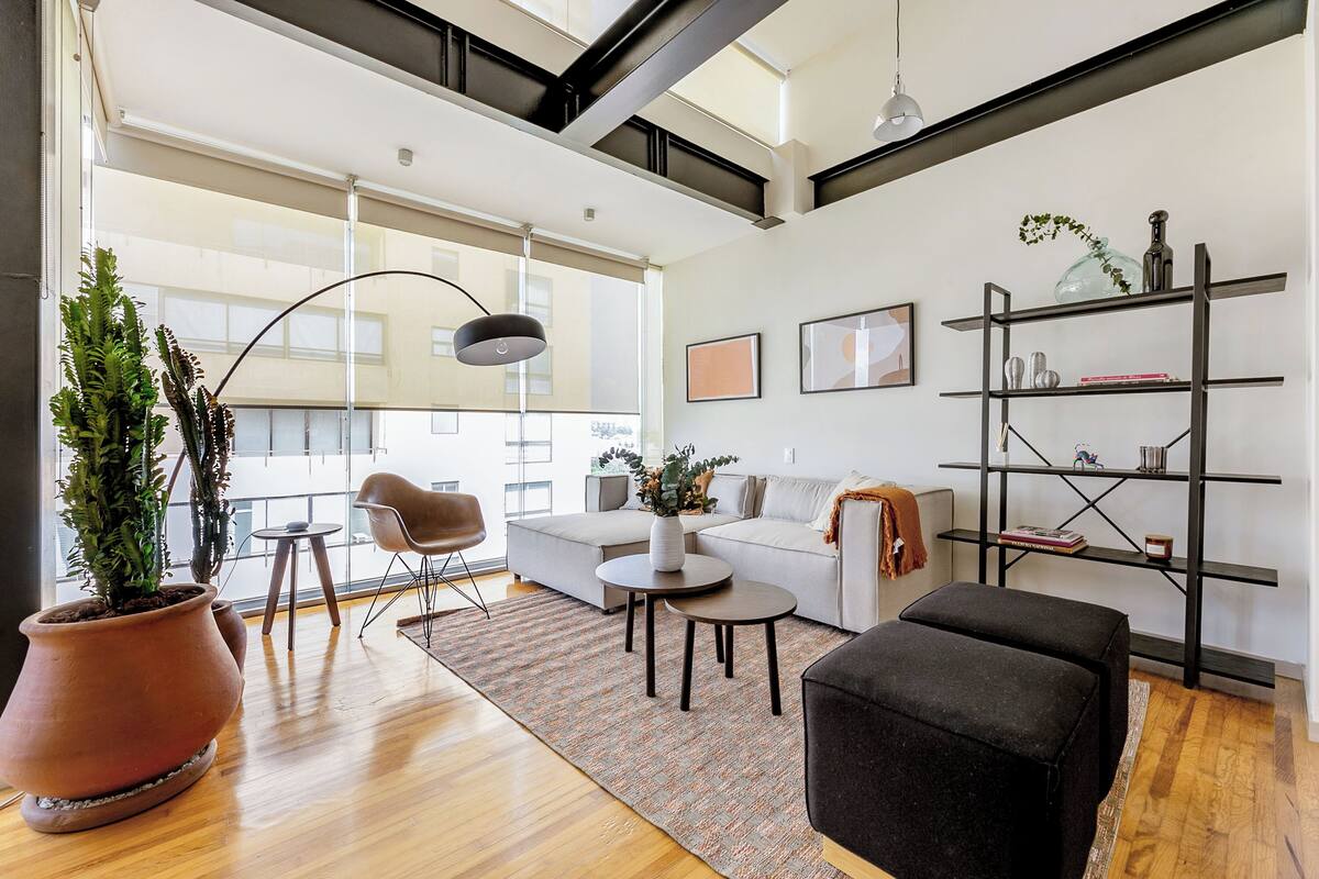 A modern living room with a sofa, ottoman, coffee table, and potted plants.