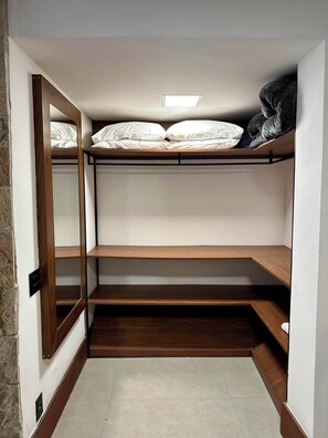A compact room with a bunk bed, a small shelf, and a mirror.