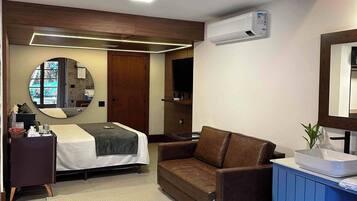 A modern bedroom with a bed, a brown leather sofa, a bathroom with a sink, and a stone wall.
