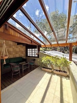 Un área de patio techada con techo de madera, asientos verdes y plantas en macetas.
