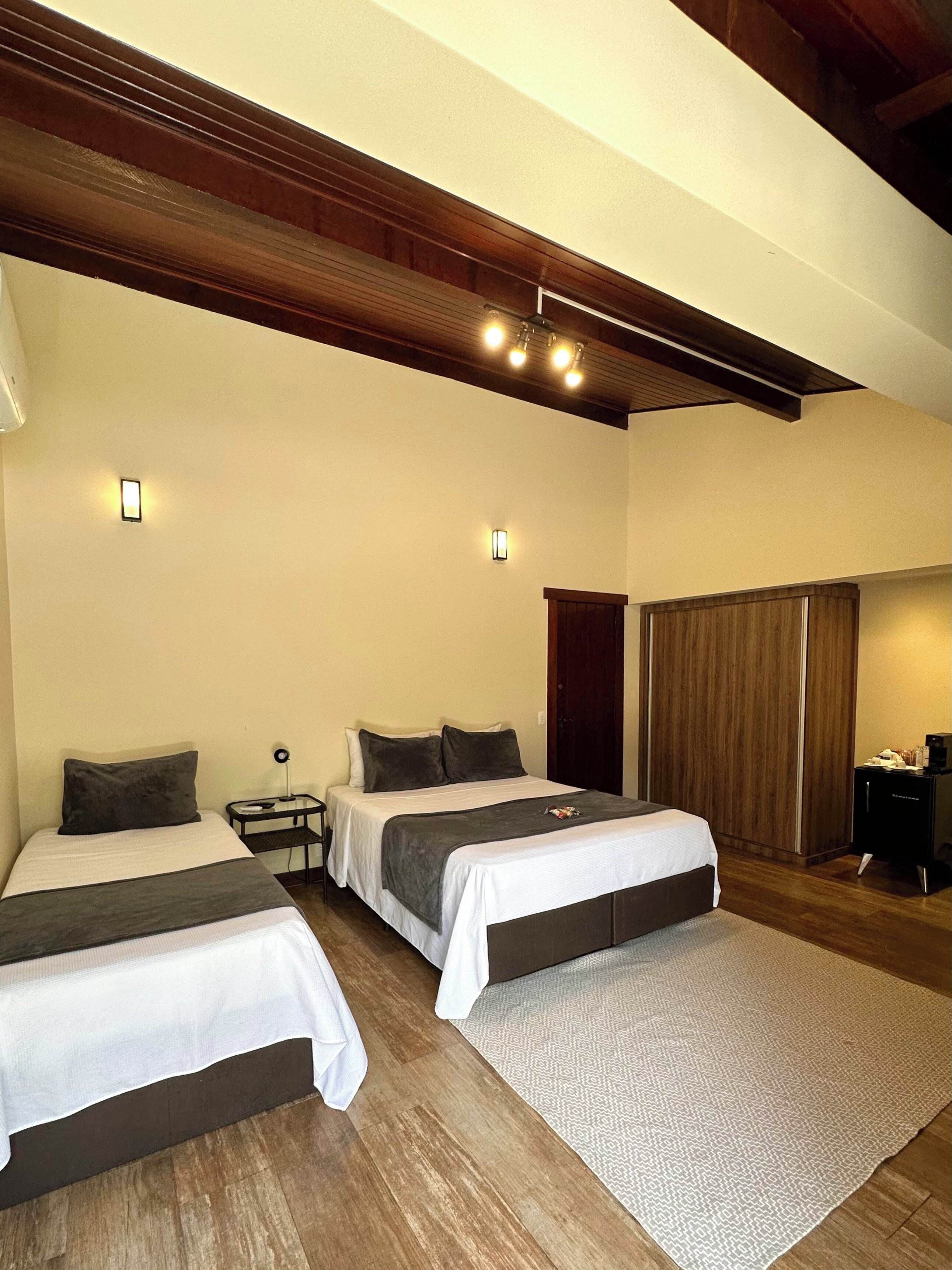 A hotel room with two beds, a wooden ceiling, and a small bedside table with a lamp.