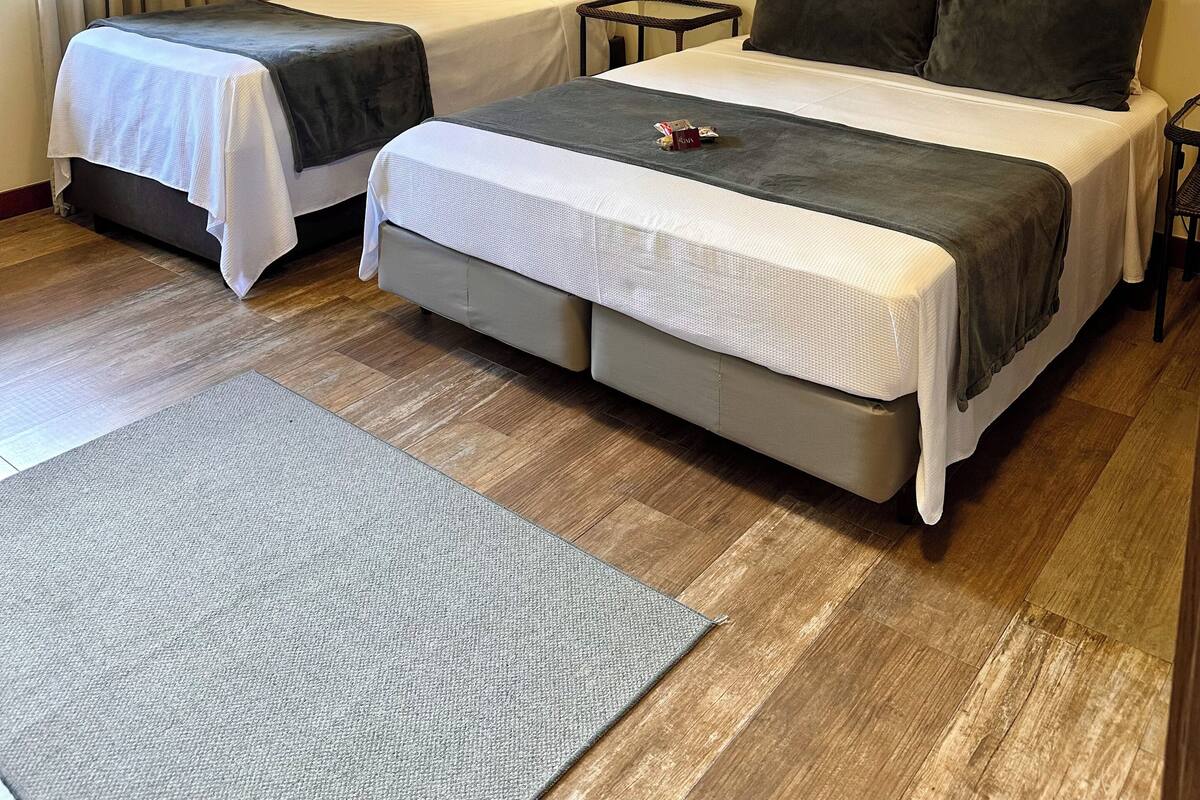 Habitación de hotel con dos camas, una mesita pequeña y una alfombra gris.