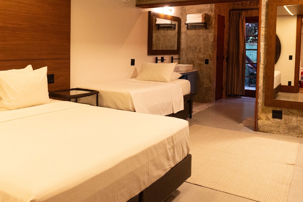 Habitación de hotel con dos camas, un baño con espejo y vista al exterior.