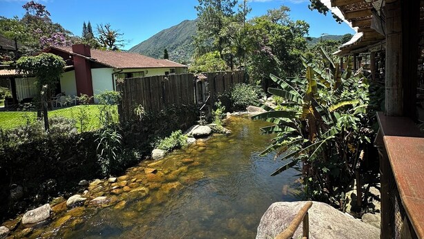 Vista despejada de un río con un puente de madera, rodeado de abundante vegetación y una montaña al fondo.
