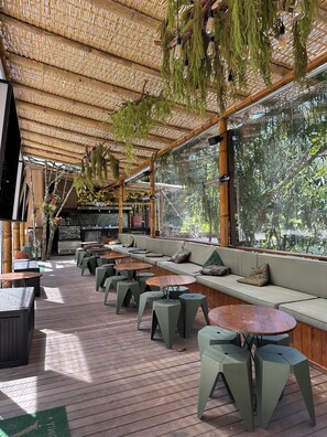 Un espace extérieur aménagé avec des sièges, un plafond en bambou, des bancs rembourrés et des tables.