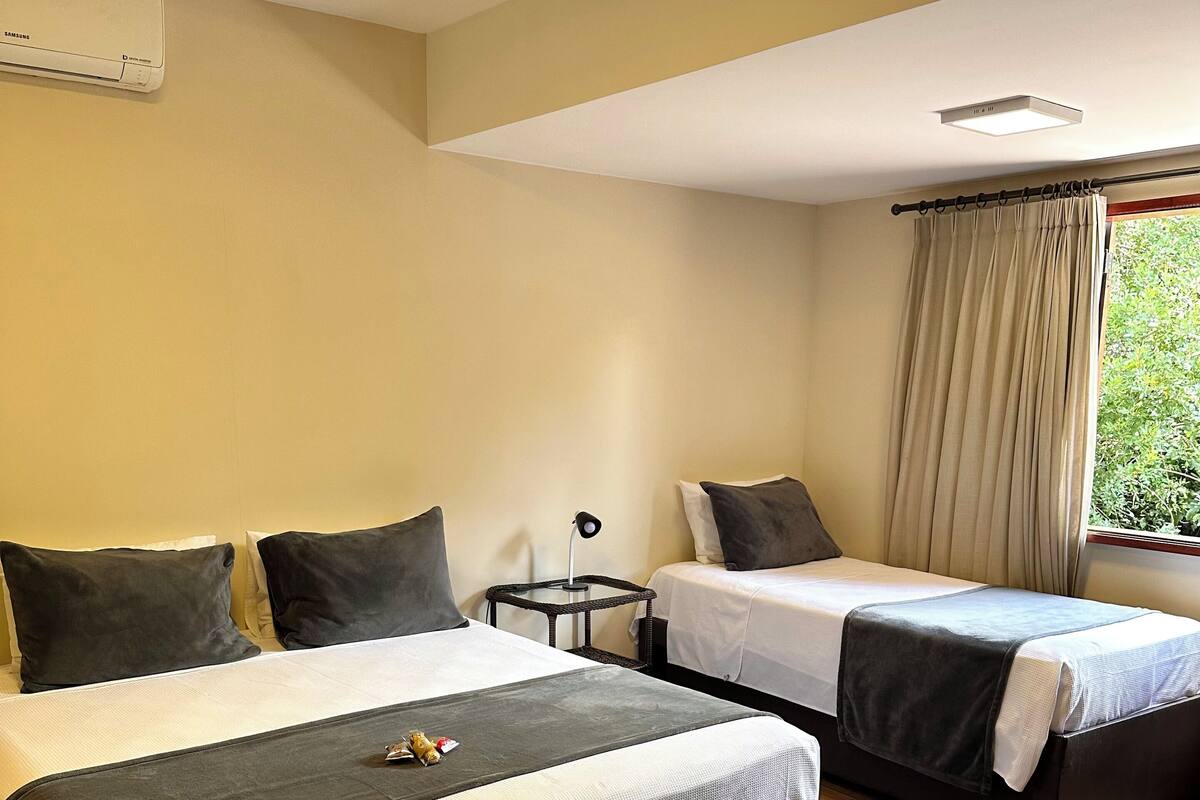 Habitación de hotel con dos camas, una mesita, una lámpara y una ventana con cortinas.
