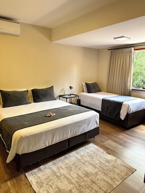 A hotel room with two beds, a small table, a lamp, and a window with curtains. - Gaia Hotelaria e Gastronomia (Teresópolis)