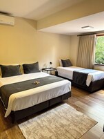 Habitación de hotel con dos camas, una mesita, una lámpara y una ventana con cortinas.