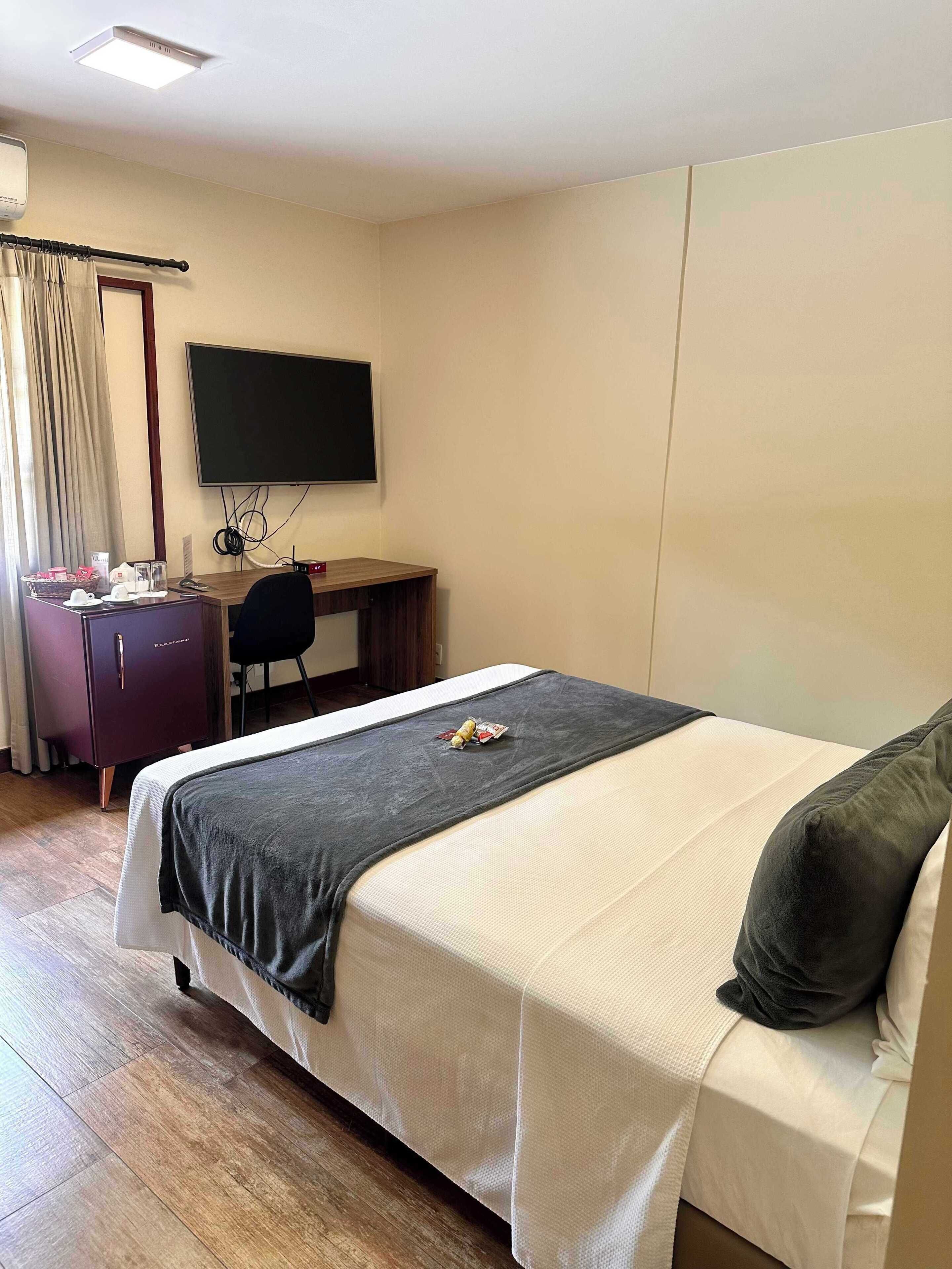 Habitación de hotel con cama, escritorio, silla, televisor y armario.