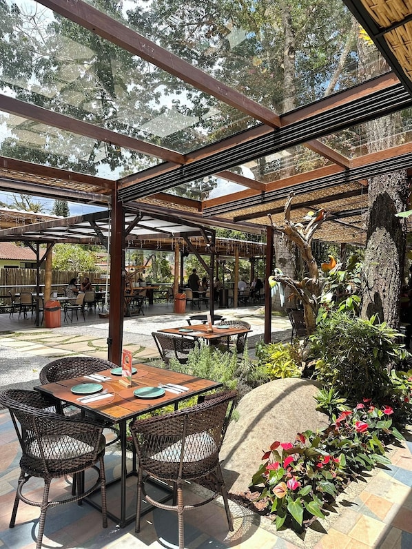 An outdoor patio area with tables and chairs, surrounded by greenery and trees.