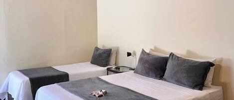 A hotel room with two beds, a ceiling fan, a wall-mounted air conditioner, and a bedside table with a lamp.