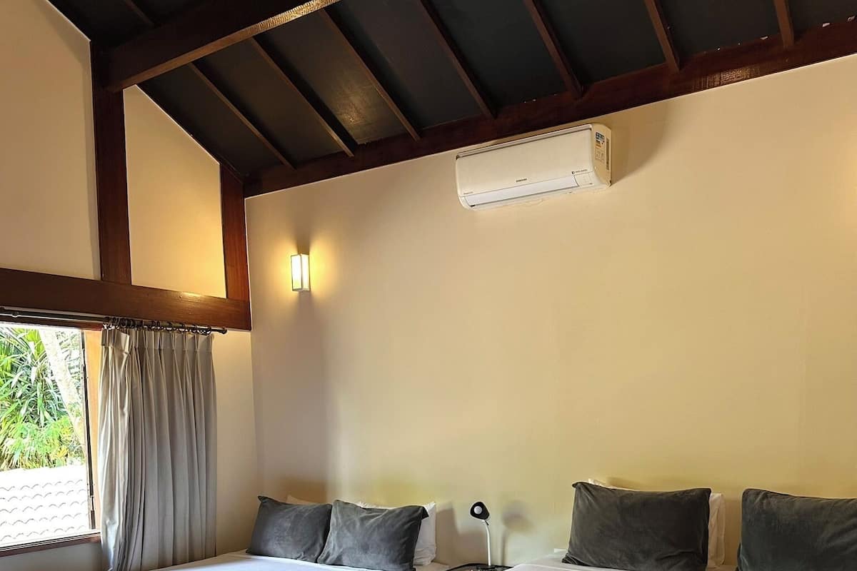 Una habitación con dos camas, ventilador de techo, aire acondicionado de pared y una ventana con cortinas.