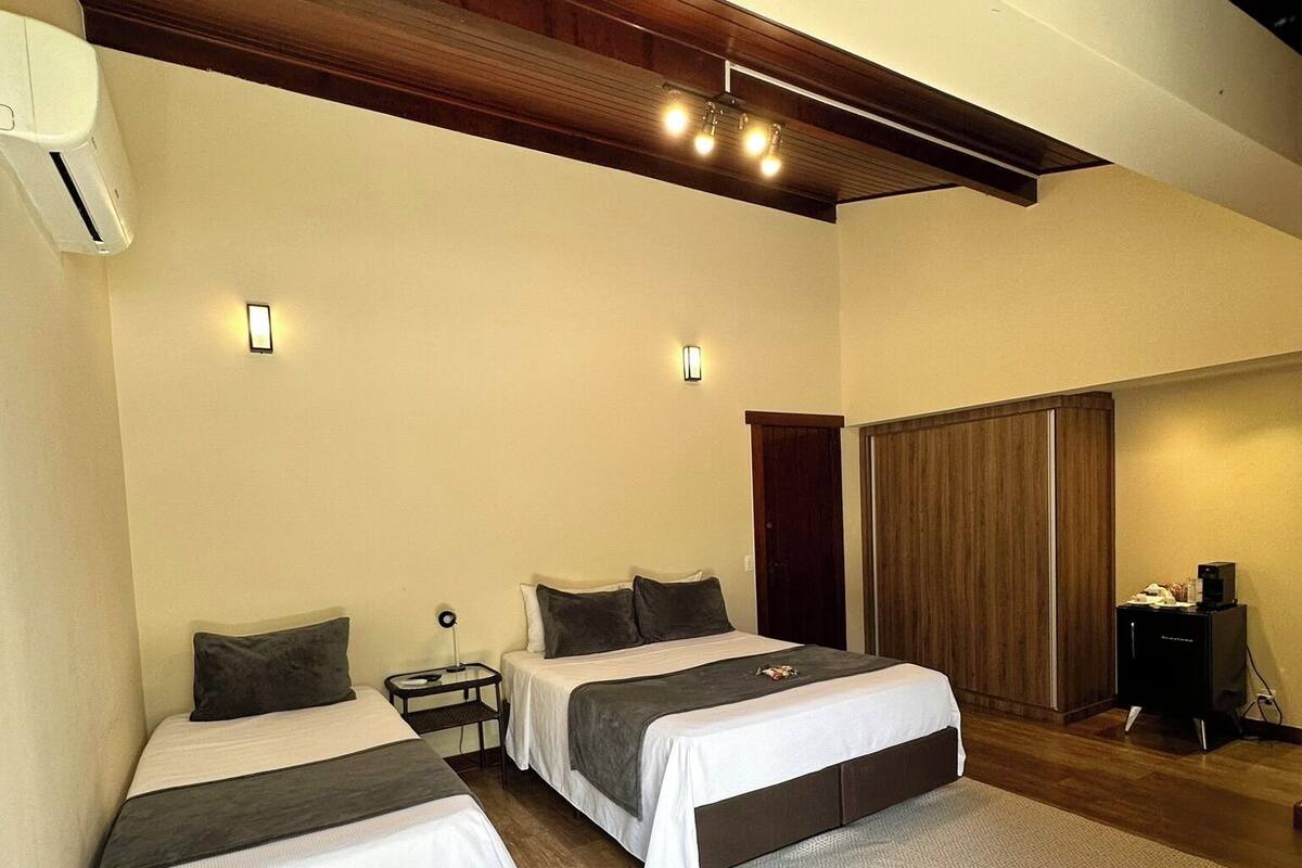 Habitación de hotel con dos camas, piso de madera, techo con vigas a la vista y un pequeño escritorio con lámpara.