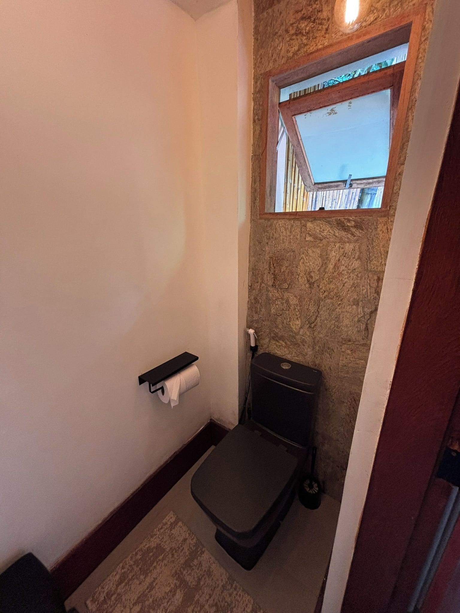 A compact bathroom with a toilet, a towel holder, and a small window.