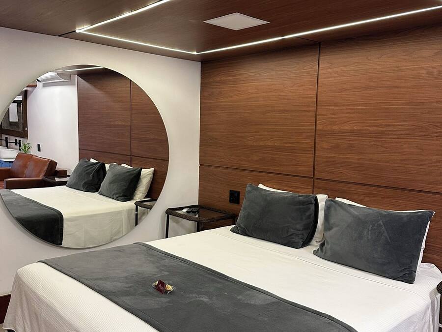 A modern hotel room with a large bed, a round mirror, and a wooden panel wall.