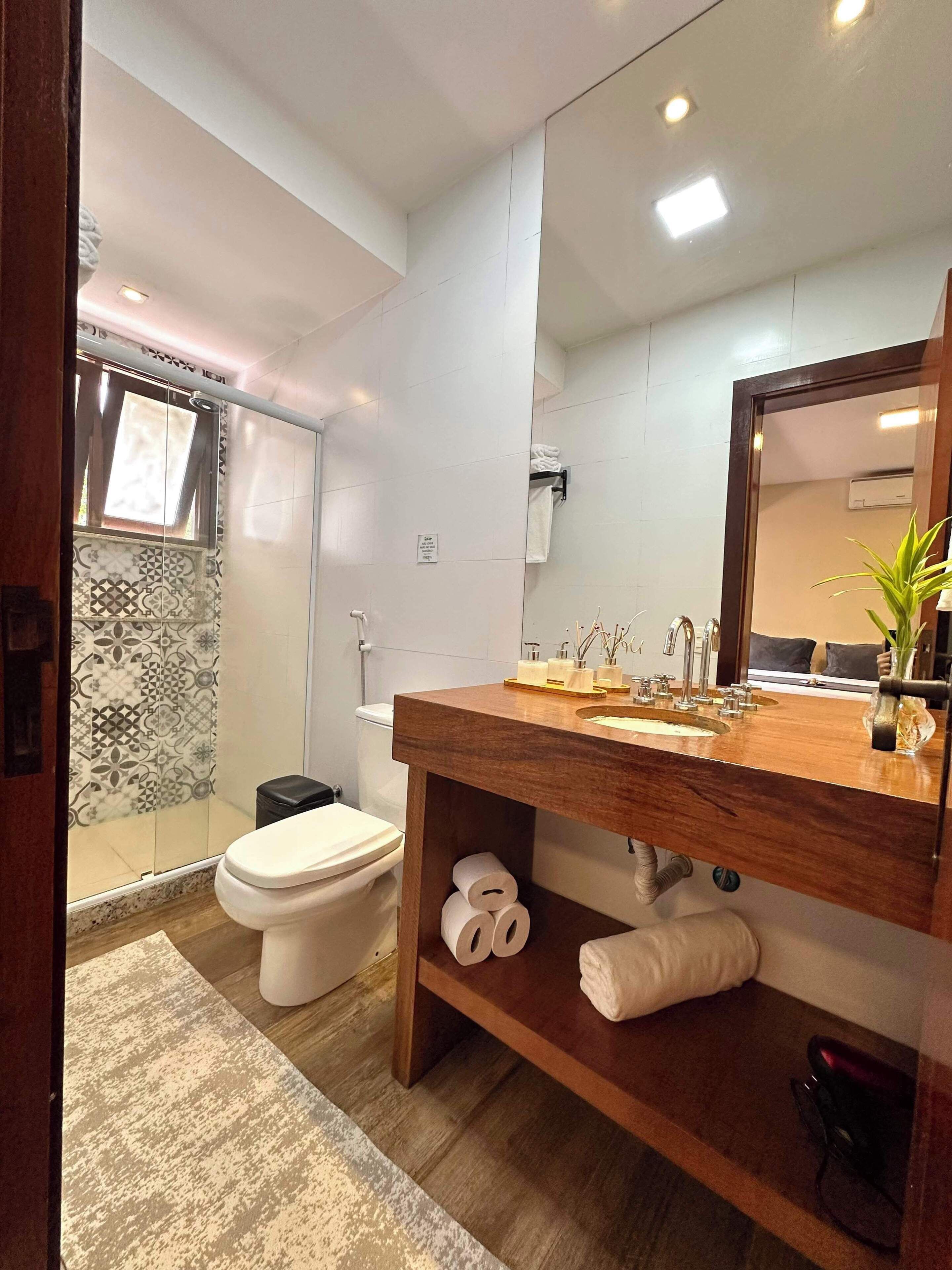 Ein modernes Badezimmer mit einem Holzbadezimmerunterschrank, einem großen Spiegel und einer Duschkabine.