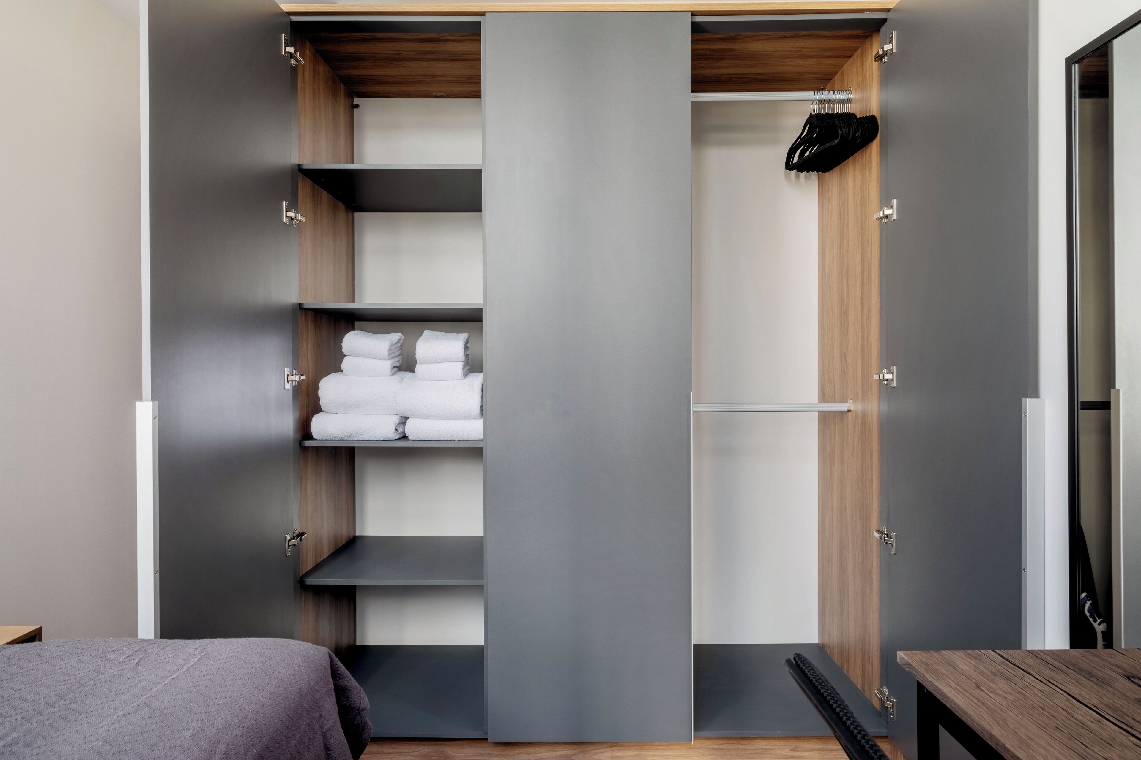 A modern bedroom with a bed, a wooden bench, and a built-in wardrobe with shelves.