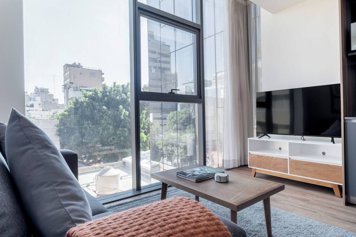 Ein modernes Wohnzimmer mit großem Fenster, einer Couch, einem Couchtisch und einer TV-Konsole.