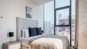 A modern hotel room with a large bed, a bedside table with a lamp, a view of the city through a large window, and a framed picture on the wall. - Blueground Josefa by Urbanistas CDMX (Mexico City)