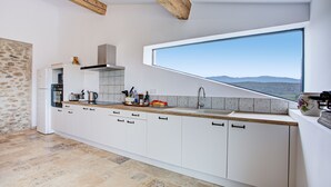 A modern kitchen with white cabinets, a large window, and a stone wall.