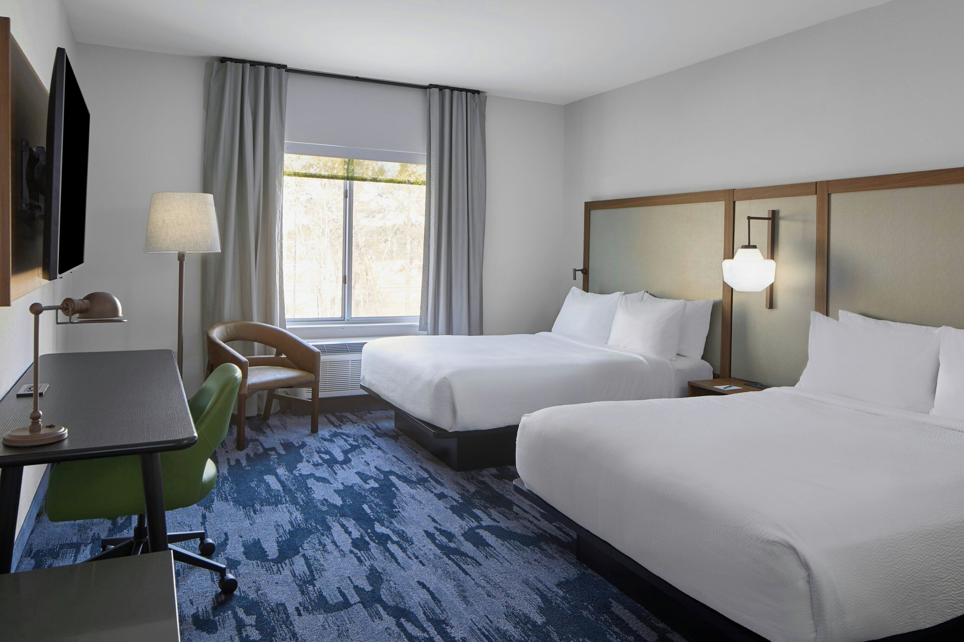 A hotel room with two beds, a desk with a chair, a TV, and a window with curtains.