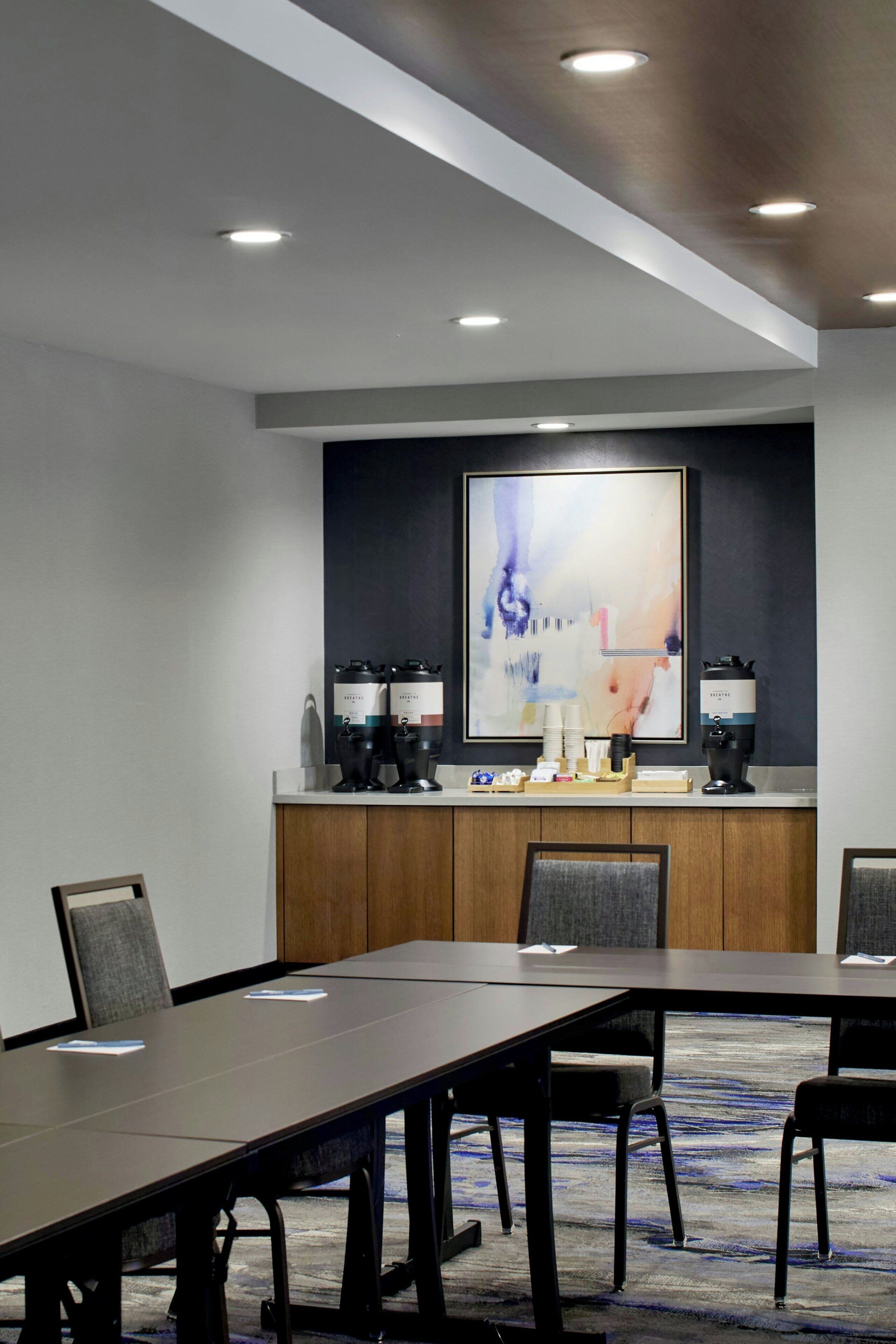 A conference room with a long table, chairs, a coffee station, and a large abstract painting on the wall.