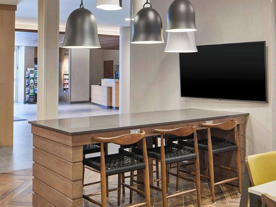 Un área de cocina moderna con una isla central, taburetes de bar, iluminación colgante y un televisor de pantalla plana montado en la pared.