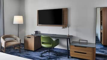 Una habitación de hotel con cama, escritorio, silla, televisor, lámpara y espejo.