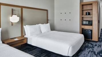 A hotel room with a large bed, a bedside table with a lamp, a built-in microwave, and a small refrigerator.