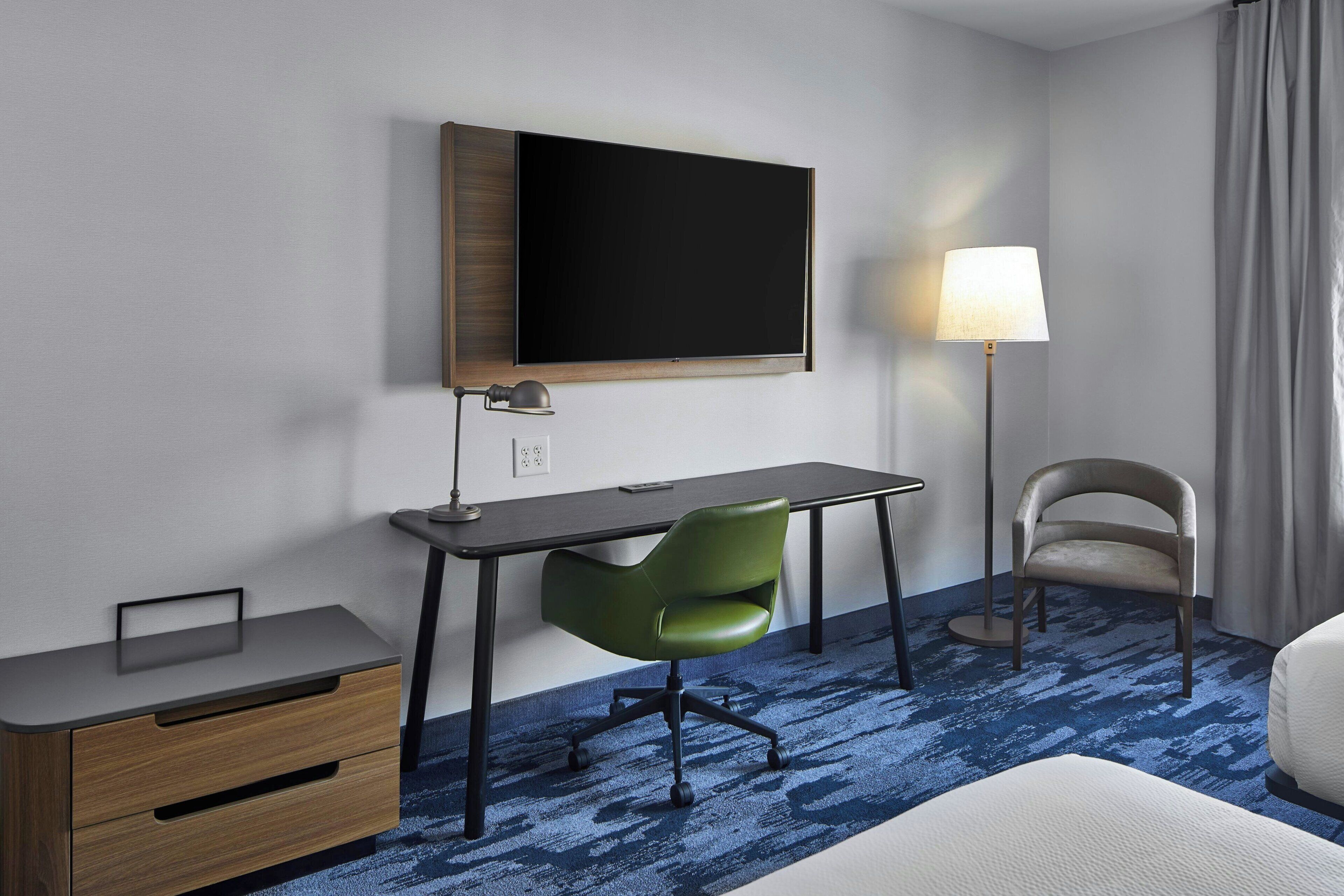 Habitació d'hotel amb escriptori, cadira verda i televisió de pantalla plana penjada a la paret.