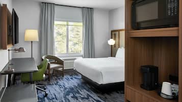 A hotel room with a bed, a desk, a chair, a coffee maker, and a television.