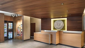 A modern reception area with a wooden reception desk, a decorative wall piece, and vending machines. - Fairfield By Marriott Inn & Suites Cornelia (Cornelia)