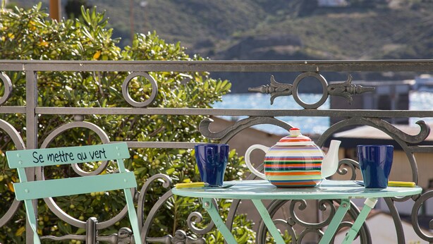 A metal railing with a sign that reads "Se mettre au vert" and a table with a striped teapot, a blue cup, and a yellow cup.