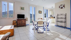 A spacious room with a bed, a TV, a dining table with chairs, and a kitchen area.