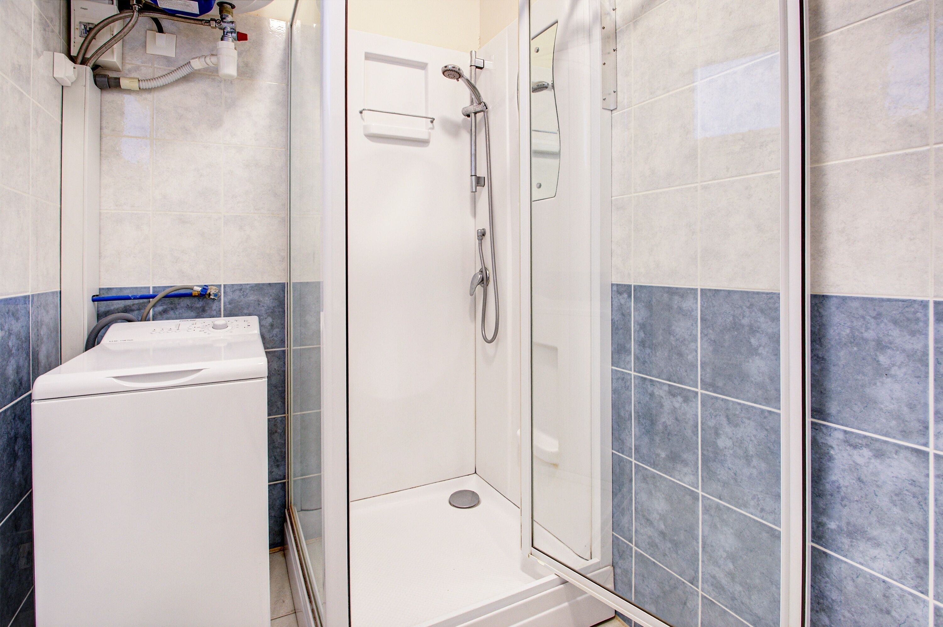 Un espace douche doté d’une porte en verre, d’un lave-linge blanc et de murs carrelés.